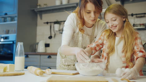 Happy-cheerful-mother-with-her-cute-schoolgirl-daughter-talking-and-laughing-while-making-a-daugh-for-cookies-and-muffins-in-the-cozy-modern-kitchen.-Indoors